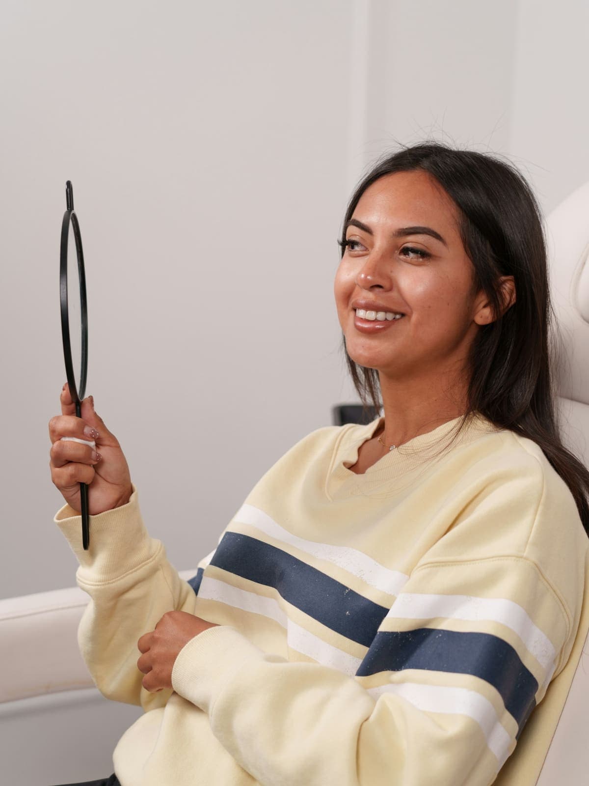 Smiling client holding a hand mirror after her treatment